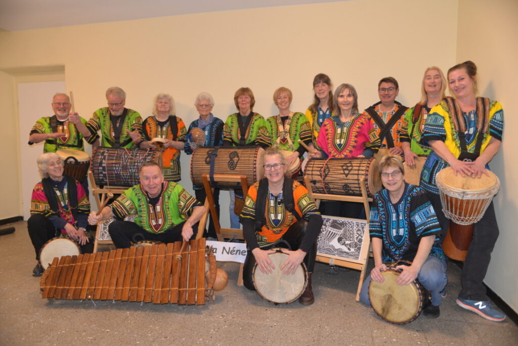 Trommelgruppe Ya Ya Néné in bunten afrikanischen Gewändern mit Djemben, Basstrommeln und Balafon beim Gruppenfoto.